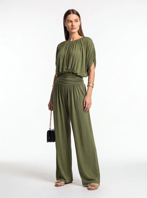 Jamota olive green jumpsuit with gathered neckline and ruched waist, wide-leg pants; model wearing gold bracelets.