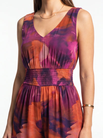 Elegant tie-dye women's jumpsuit with V-neck and smocked waistband in purple, pink, and orange hues.