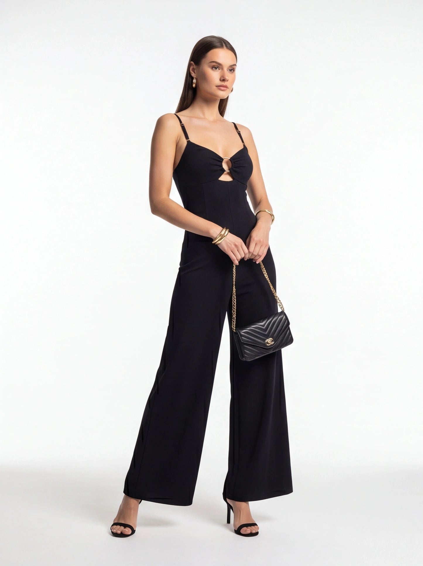 Jamota black jumpsuit with adjustable straps, front ring detail and wide-leg silhouette, paired with a quilted handbag.