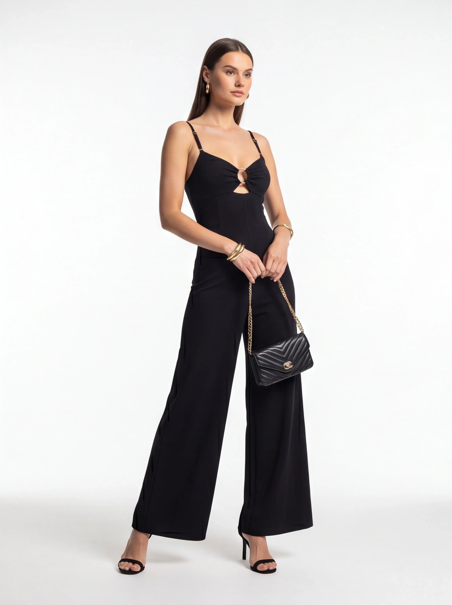Jamota black jumpsuit with adjustable straps, front ring detail and wide-leg silhouette, paired with a quilted handbag.