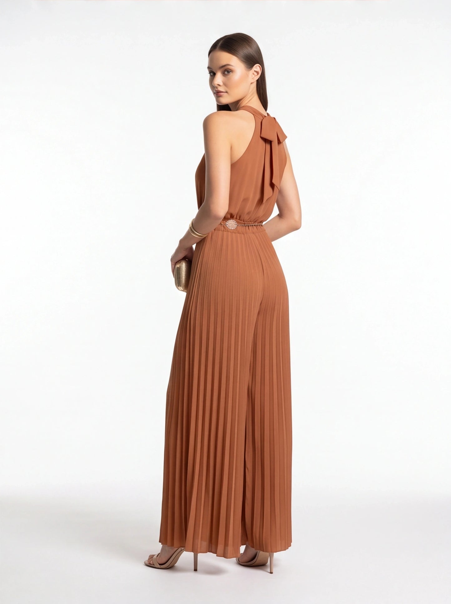 Jamota terracotta jumpsuit with pleated wide-leg, halter neck and back bow, and waist belt with round buckle.