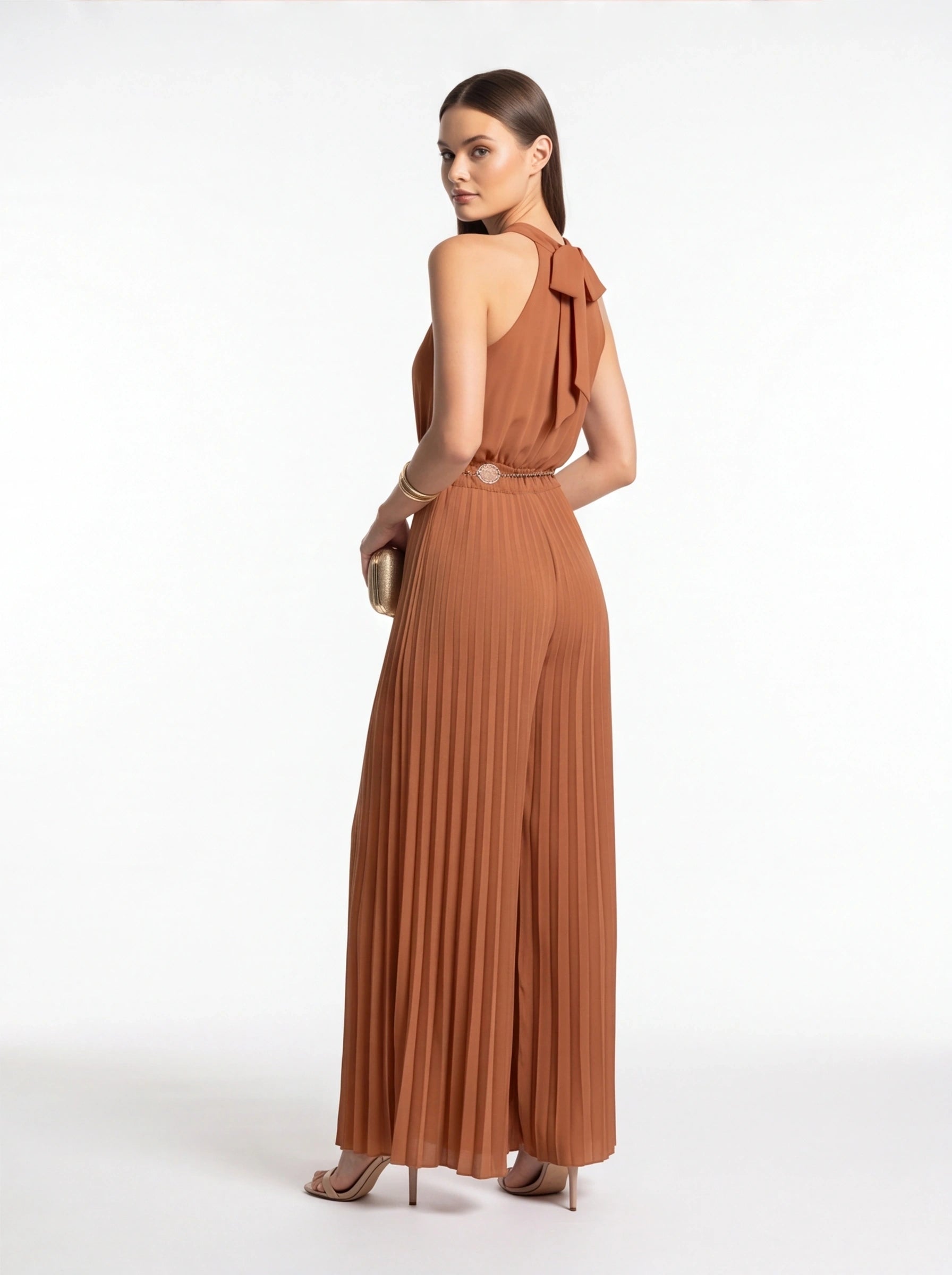 Jamota terracotta jumpsuit with pleated wide-leg, halter neck and back bow, and waist belt with round buckle.
