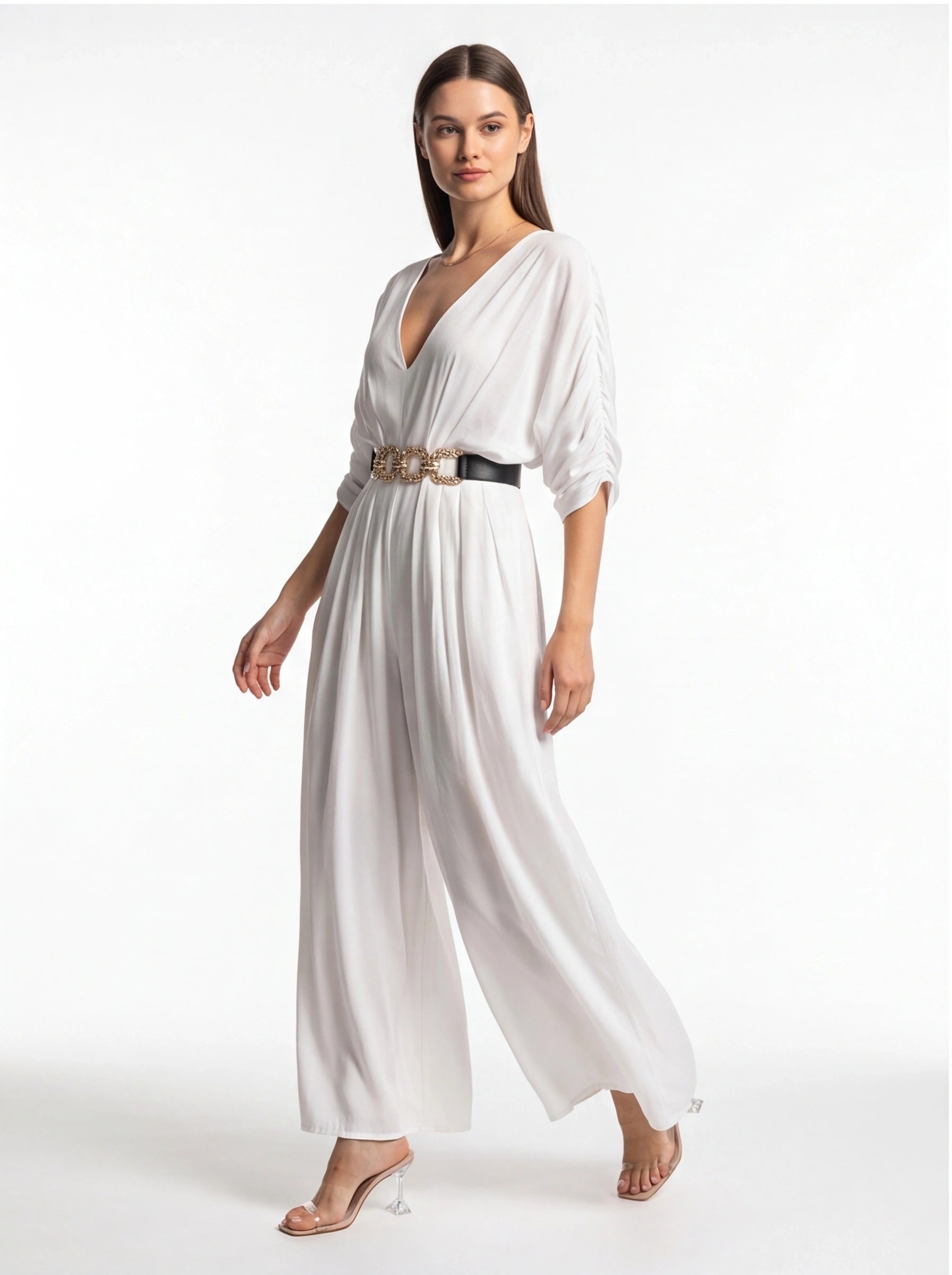 Jamota white jumpsuit with wide legs and deep V-neck, cinched by a black belt with a gold chain.