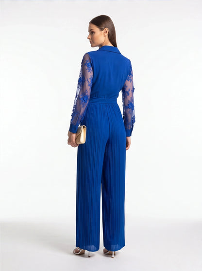 Jamota blue jumpsuit with sheer floral lace sleeves, belt at waist, and pleated wide legs.